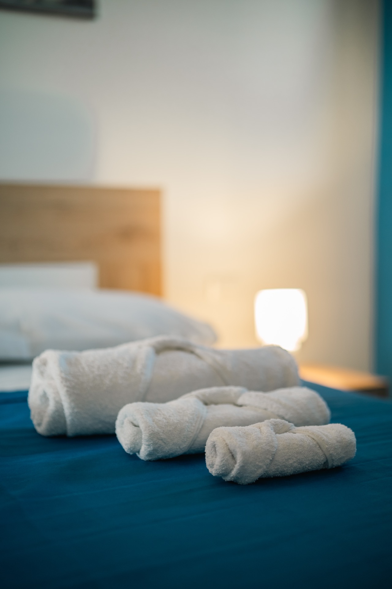 Dettaglio degli asciugamani arrotolati sul letto blu della Dimora Blu con lampada accesa